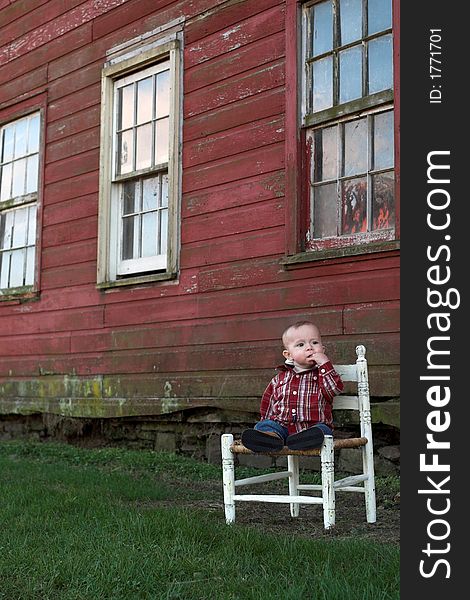 Image of baby boy sitting on a chair in front of a red farm building. Image of baby boy sitting on a chair in front of a red farm building