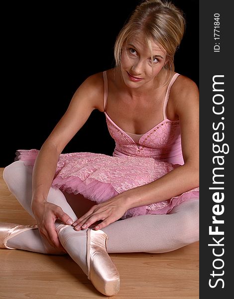 Ballerina with pink tutu siting on ground fastening shoes (looking up). Ballerina with pink tutu siting on ground fastening shoes (looking up)