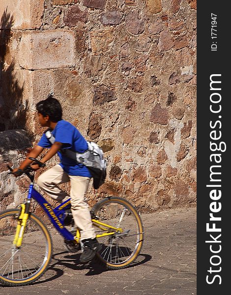 Mexican boy on a bike with a stone wall in the back in the town of Alamos in the northern state of Sonora in Mexico, Latin America