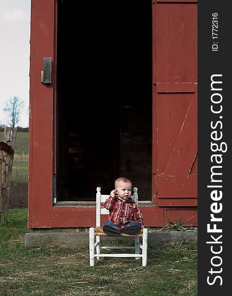 Image of baby boy sitting on a chair in front of a red farm building. Image of baby boy sitting on a chair in front of a red farm building