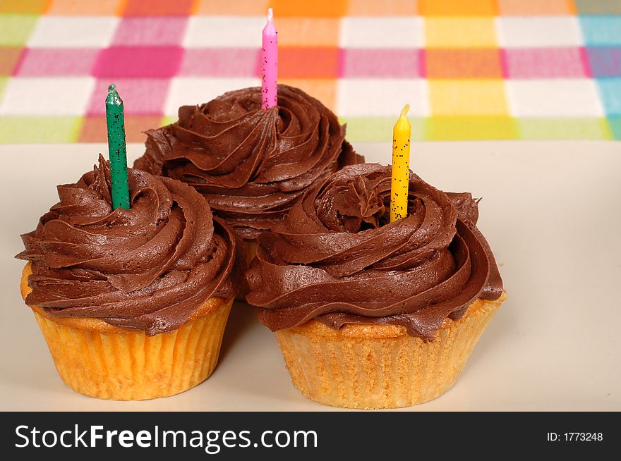 Three delicious chocolate frosted cupcakes with candles. Three delicious chocolate frosted cupcakes with candles