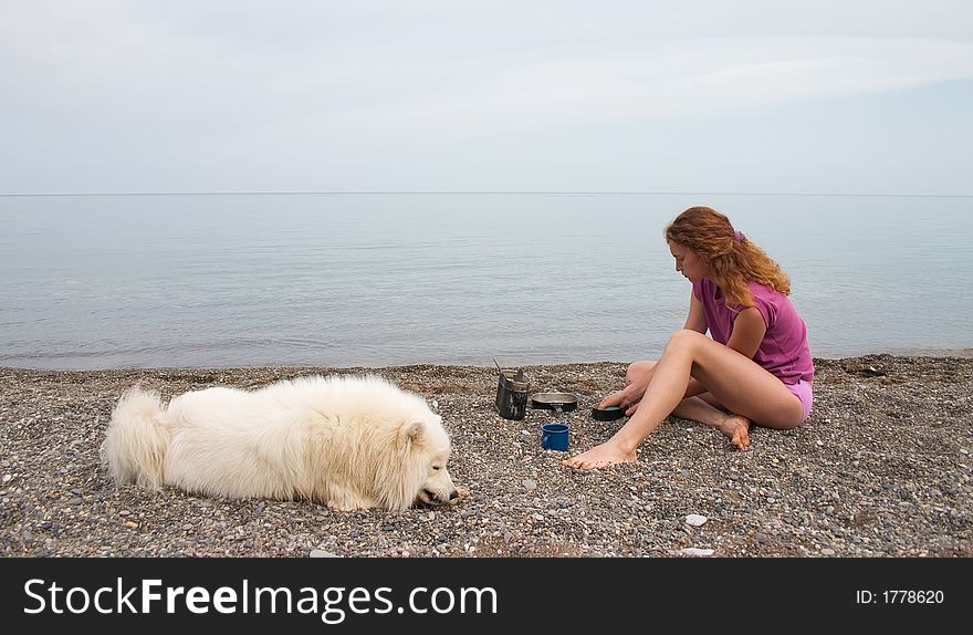 Girl washing dishes at the seashore and samoyed dog lying nearby. Girl washing dishes at the seashore and samoyed dog lying nearby