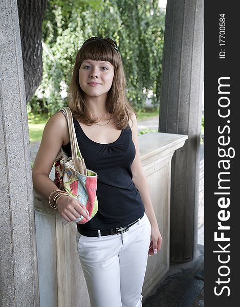 The young girl the brunette with a multi-colored bag costs between stone columns