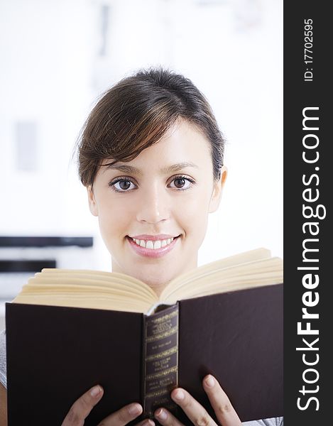 Woman reading book in home interior, smiling and looking in camera; concept of relax and entertainment. Woman reading book in home interior, smiling and looking in camera; concept of relax and entertainment