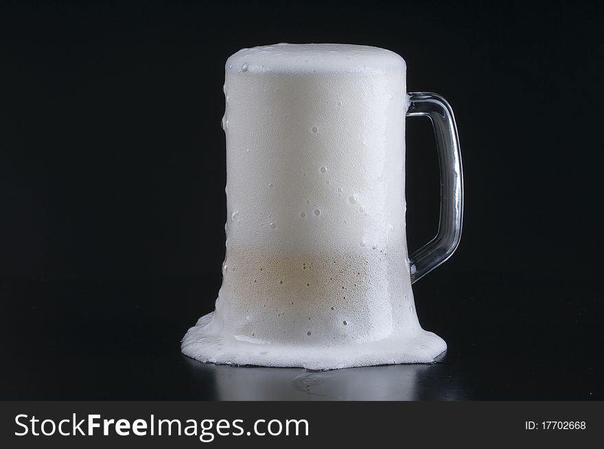 A light beer foaming over the rim of a frosty mug. A light beer foaming over the rim of a frosty mug.