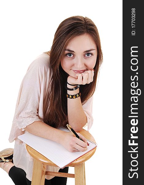 A beautiful teenager kneeling for a chair and writing in her notebook, smiling into the camera, for white background. A beautiful teenager kneeling for a chair and writing in her notebook, smiling into the camera, for white background.