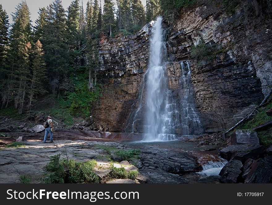 A man looks up at a waterfall in Glacier National Park.