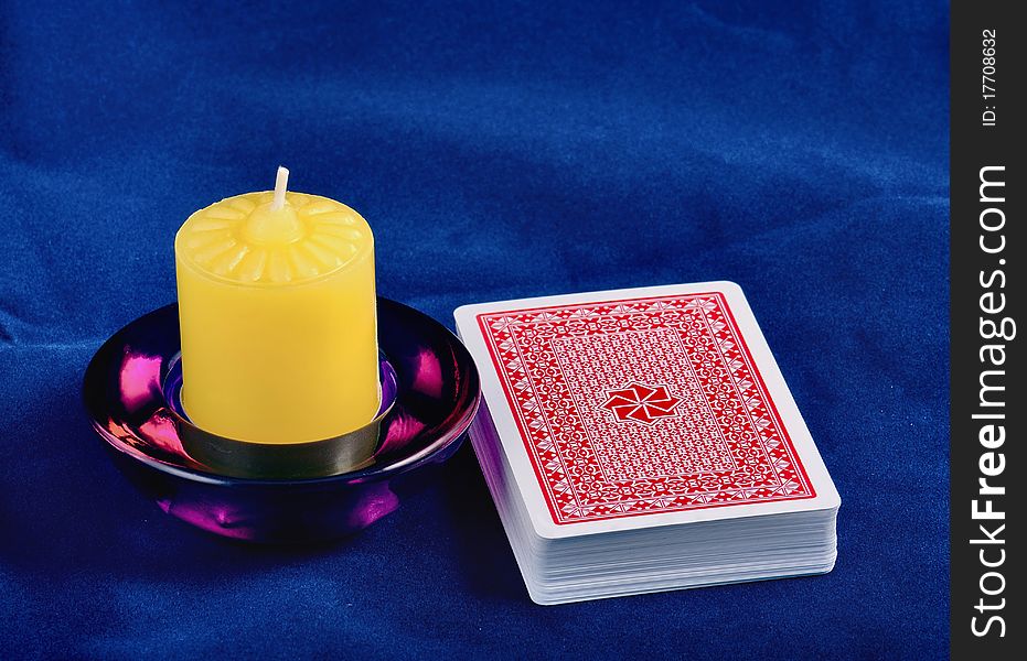 The back of a playing cards lays on a dark blue fabric, near locates a candle. The back of a playing cards lays on a dark blue fabric, near locates a candle