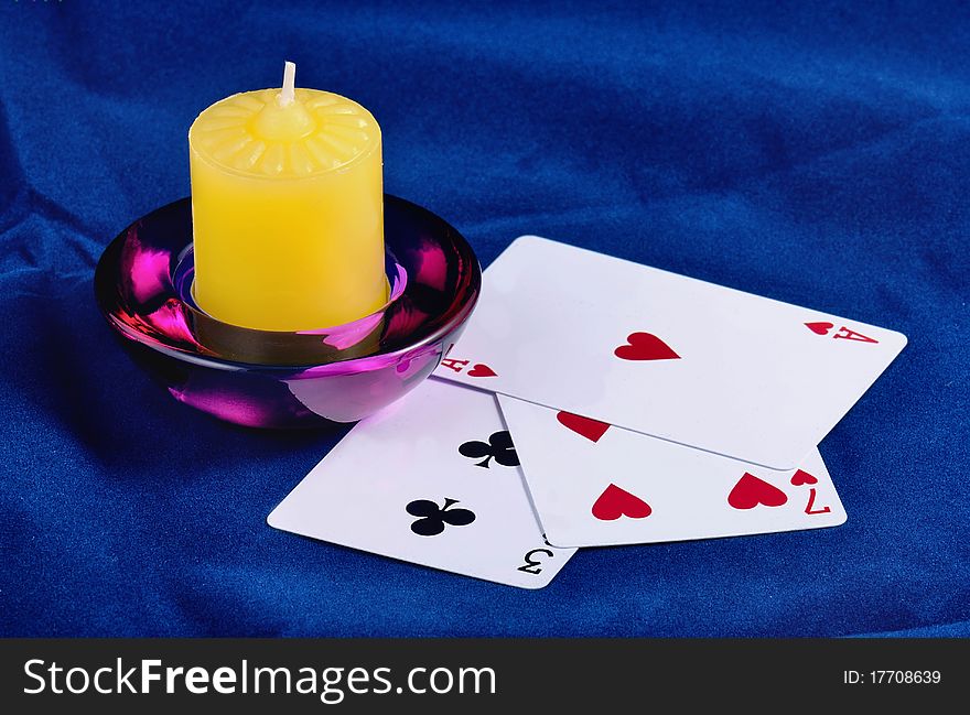 Three playing cards are opened and lays on a dark blue fabric, near locates a candle. Three playing cards are opened and lays on a dark blue fabric, near locates a candle