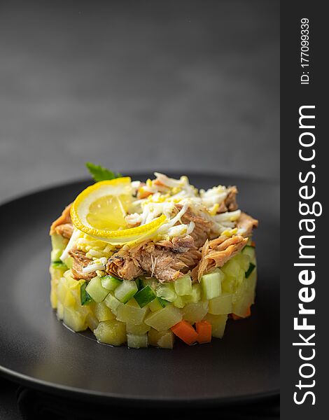 Salad with canned tuna and vegetables in culinary ring on black plate. Dark background. Beautiful serving in the restaurant