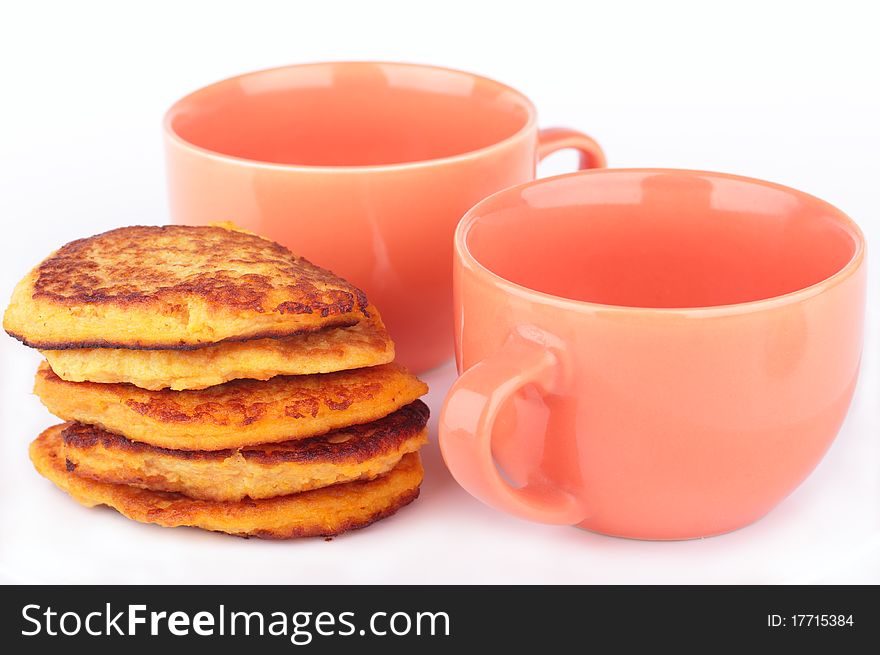 Fresh homemade pumpkin pancakes and two orange cups for breakfast isolated on white background