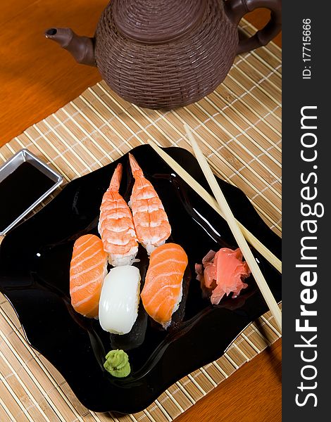 Tasty dish of assorted sushi on black plate and teapot. Tasty dish of assorted sushi on black plate and teapot