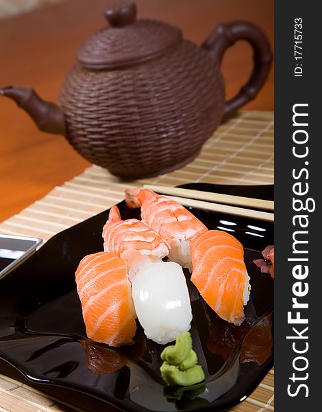 Tasty dish of assorted sushi on black plate and teapot. Tasty dish of assorted sushi on black plate and teapot