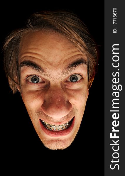 This man is clearly insane. Isolated head on black background. He is wearing braces with a big grin on this face, could be considored a mad scientist.