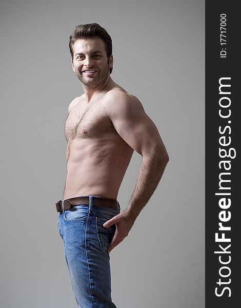 Young shirtless musculous man in jeans smiling - isolated on gray