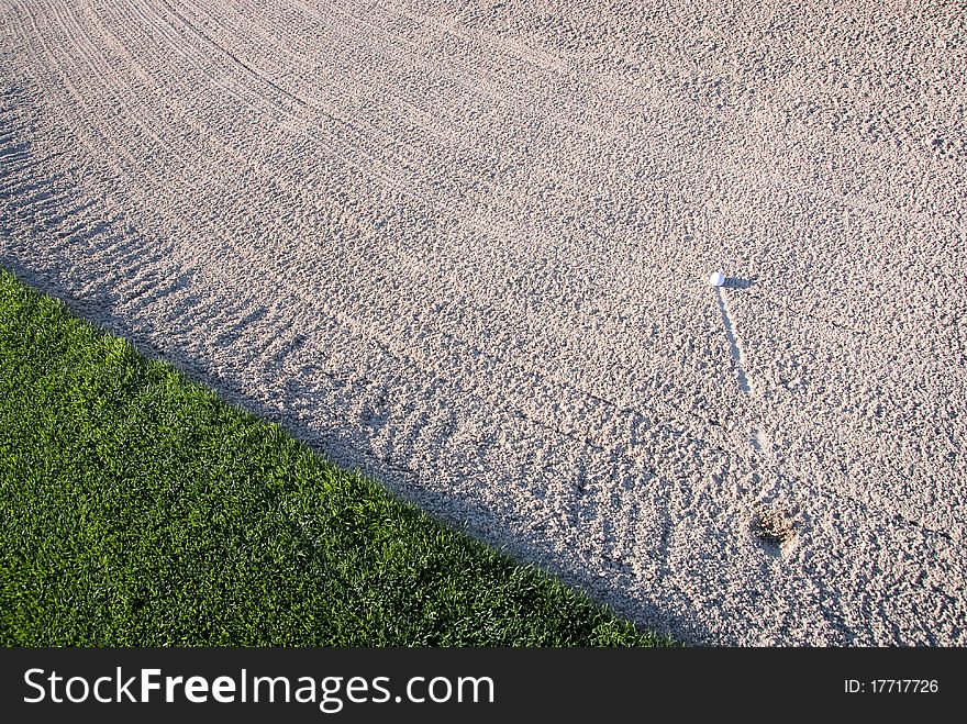 A golf ball hit into the sand trap on a golf course. A golf ball hit into the sand trap on a golf course.