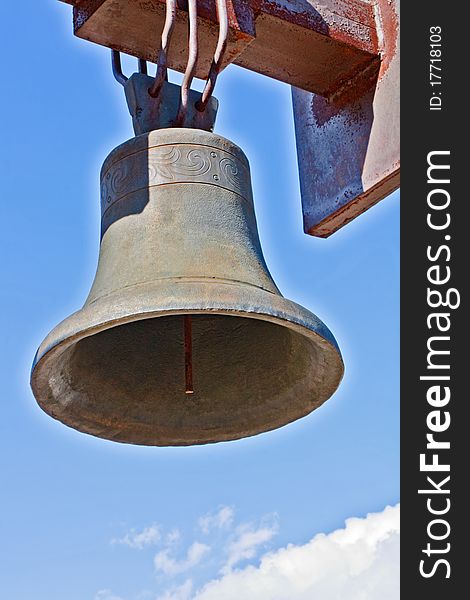 Weathered cast-iron bell against blue sky and cloud