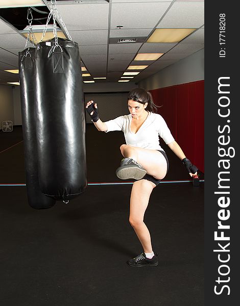 Young female kicking a punching bag in gym