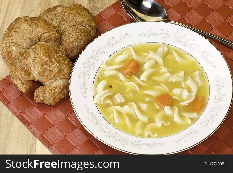 A bowl of chicken soup and croissant. A bowl of chicken soup and croissant