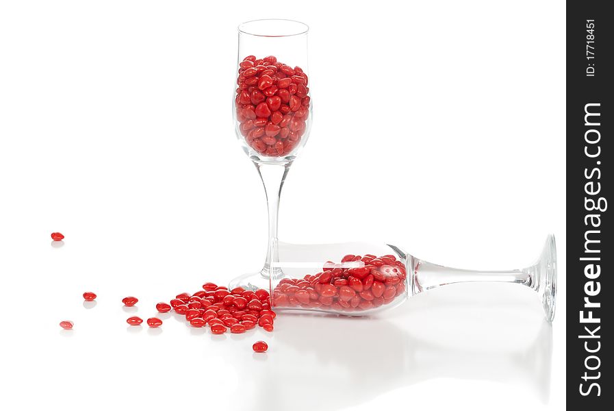 A front isolated studio view of cinnamon hearts spilled out of one of the two champagne glasses. A front isolated studio view of cinnamon hearts spilled out of one of the two champagne glasses.