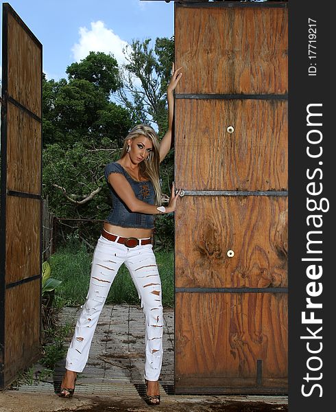 A or beuatiful young blonde hair lady is leaning against the stable doors. A or beuatiful young blonde hair lady is leaning against the stable doors