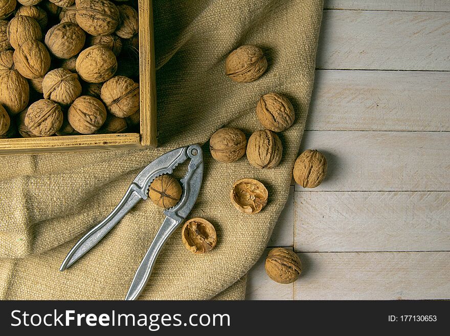 Walnuts in a wooden box, which stands on an old rustic sack, also scattered on a white table nearby is a cracker of walnut