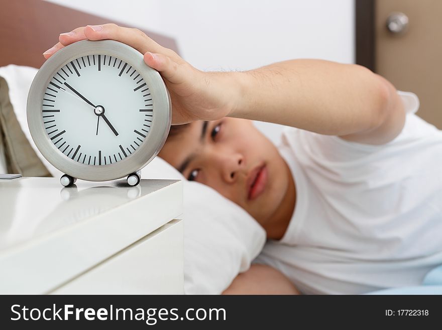 A sleepy Asian man reaching out his hand to switch off his alarm clock. A sleepy Asian man reaching out his hand to switch off his alarm clock