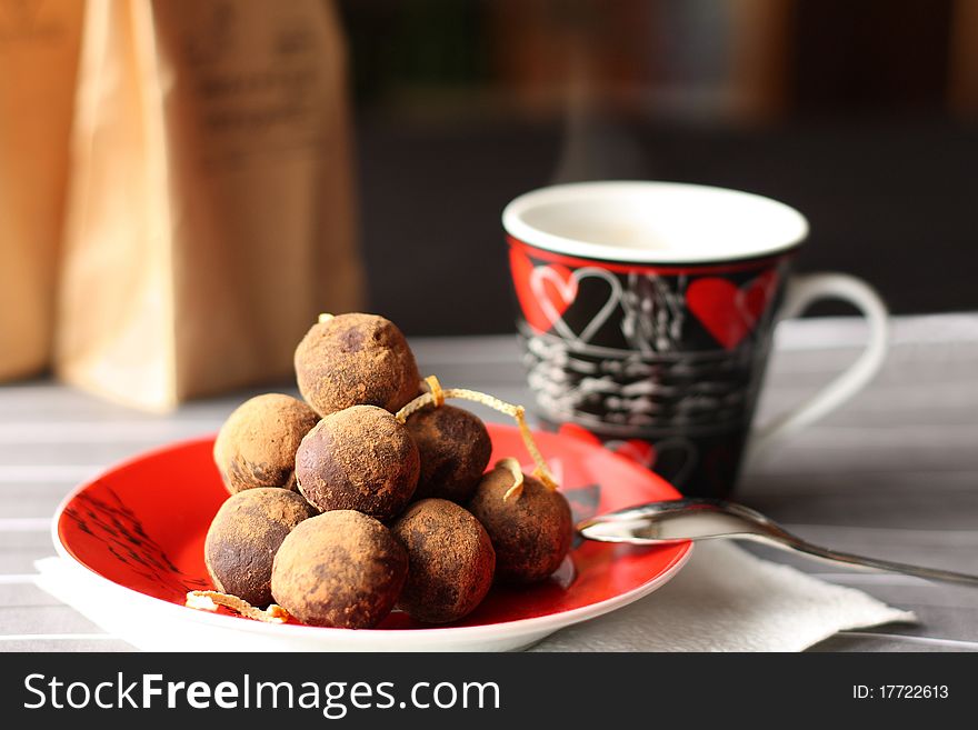 It is photo of chocolate truffles on a red saucer with a cup of coffee in the black cup with red hearts picture. It is photo of chocolate truffles on a red saucer with a cup of coffee in the black cup with red hearts picture.