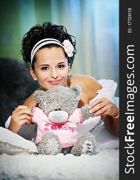 Happy bride with teddy bear on white bed