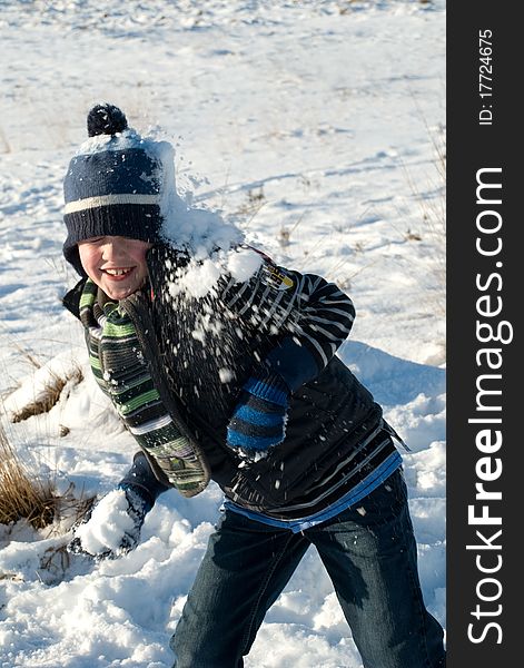 Little boy with blue winter hat having fun, throwing a snowball while getting a snowball against his head. Little boy with blue winter hat having fun, throwing a snowball while getting a snowball against his head