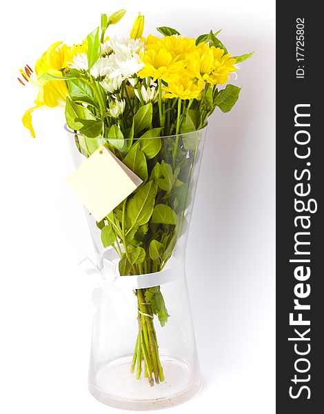 Bunch of freshly cut white carnation flowers, yellow liliums and yellow carnations arranged in a simple floral bouquet in a glass vase with a card and ribbon. Bunch of freshly cut white carnation flowers, yellow liliums and yellow carnations arranged in a simple floral bouquet in a glass vase with a card and ribbon