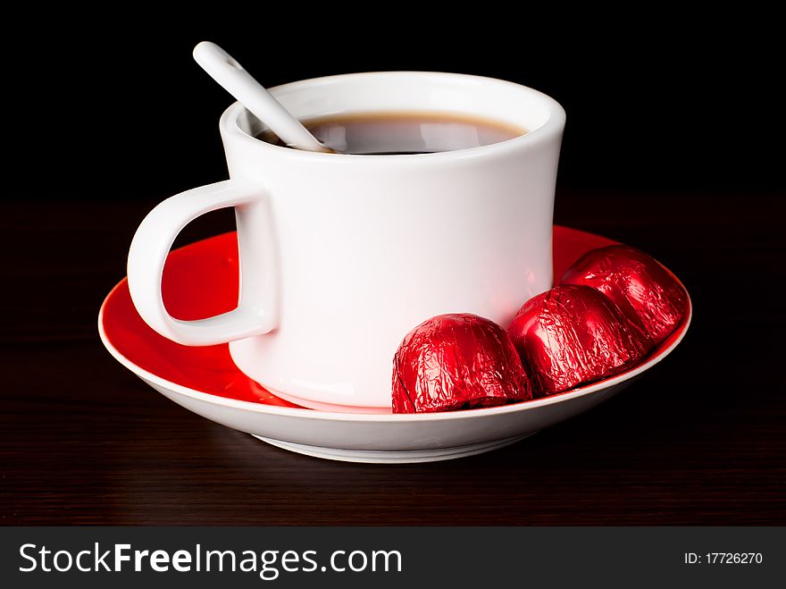 A cup of tea with swetts on the table. Black background. Studio shot. A cup of tea with swetts on the table. Black background. Studio shot.