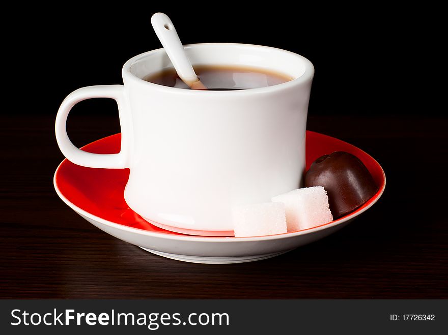 A cup of tea with swetts on the table. Black background. Studio shot. A cup of tea with swetts on the table. Black background. Studio shot.