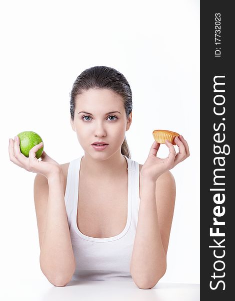 Young beautiful girl holding a green apple and cake on a white background. Young beautiful girl holding a green apple and cake on a white background