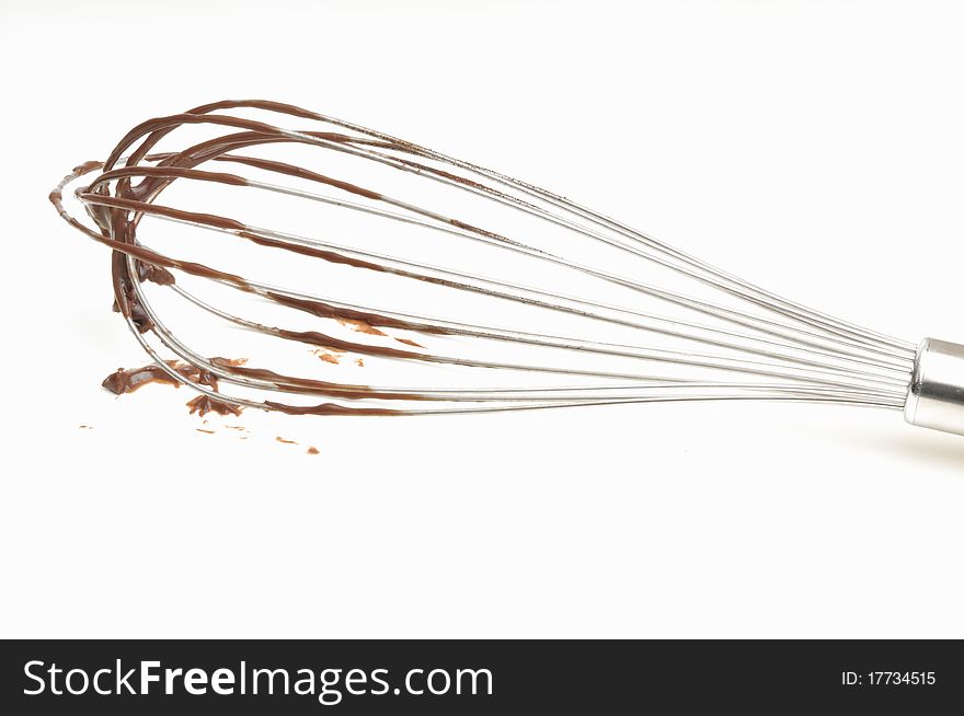 Whisk with chocolate cream on a white background