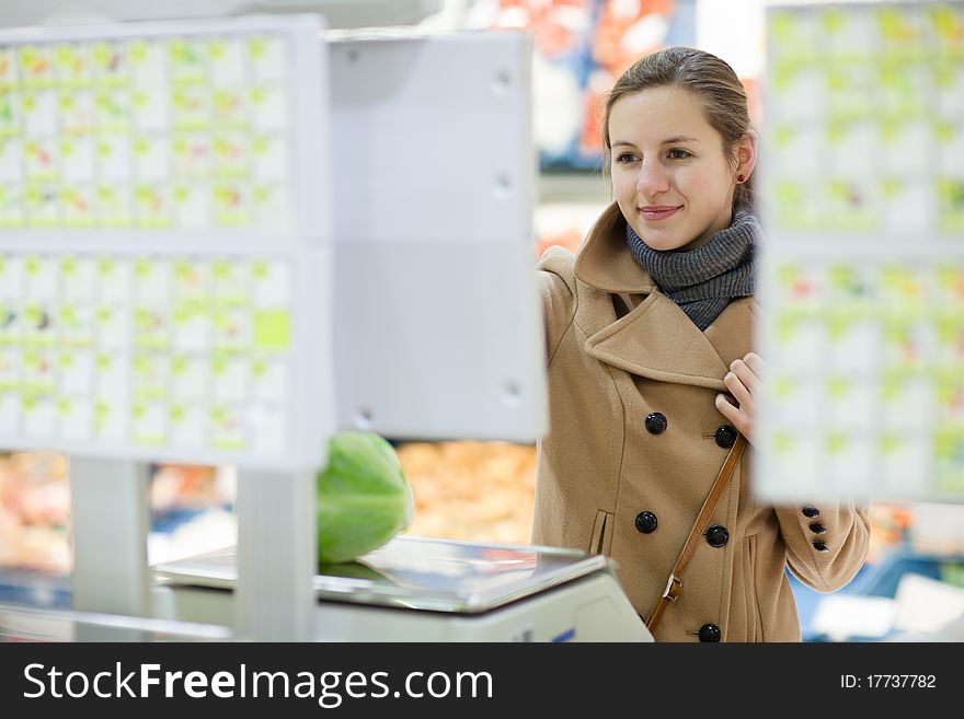 Beautiful young woman shopping for fruits and vegetables in produce department of a grocery store/supermarket - buying bananas (shallow DOF; color toned image)