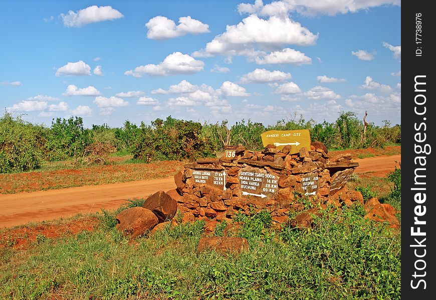 View of african savannah with red land and blue sky with the main road and directions for tented camp. View of african savannah with red land and blue sky with the main road and directions for tented camp