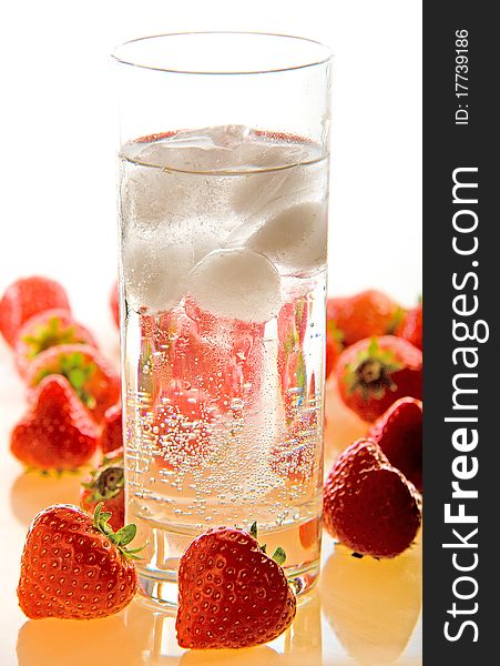 A glass of sparkling water and ice on a white background and strawberries