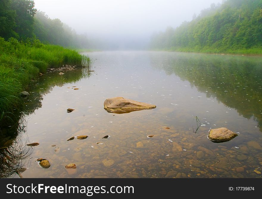 Mountain river and forest in fog at dawn. Stones in the foreground in the water