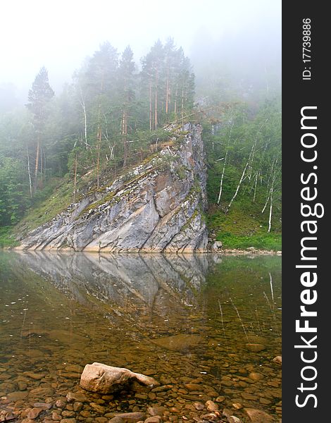 Mountain river and forest in fog at dawn. Stones in the foreground in the water