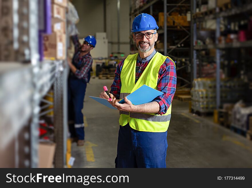 Warehouse Manager Writing On Clipboard In A Large Warehouse