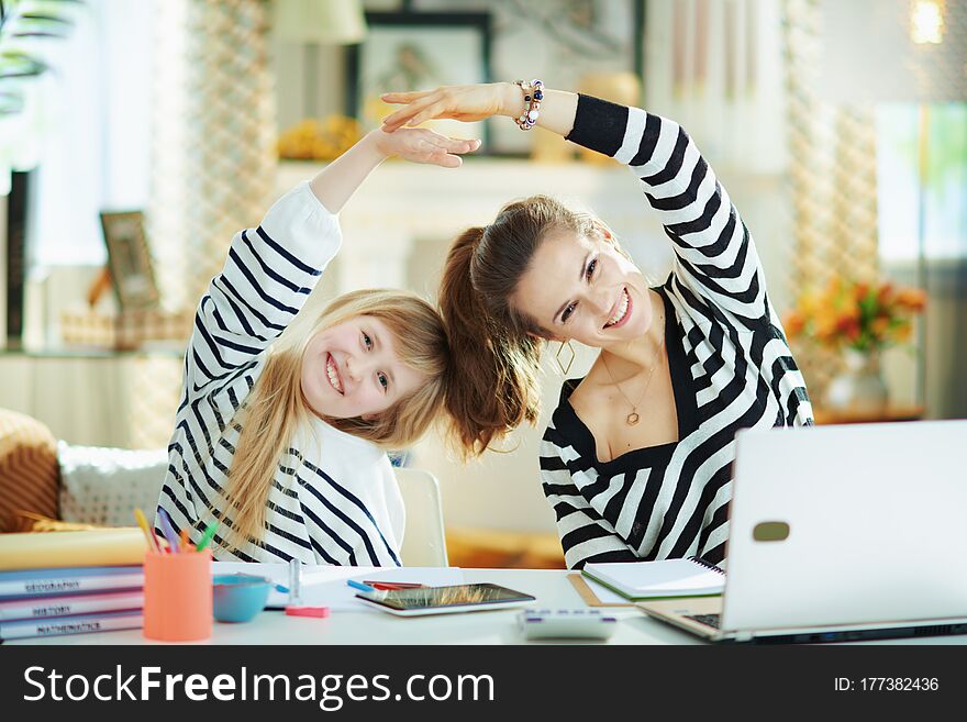 Smiling young mother and daughter in striped sweaters in home office in the modern living room in sunny day stretching. Smiling young mother and daughter in striped sweaters in home office in the modern living room in sunny day stretching