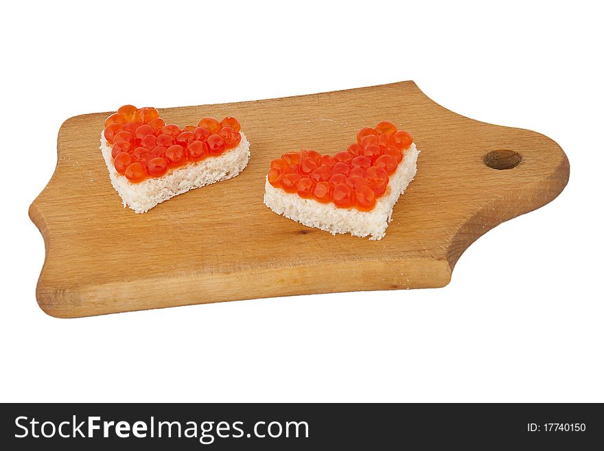 Two pieces of bread in the form of a heart with red caviar on wooden plank on white background. Two pieces of bread in the form of a heart with red caviar on wooden plank on white background