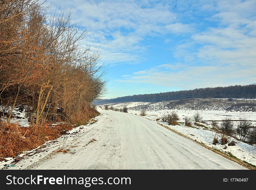 Snowy road near frozen forest in a sunny winter day