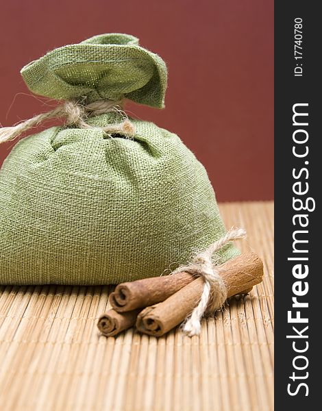 Green bag filled with spices corded near cinnamon sticks