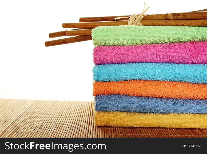 Lots of colorful bath towels stacked on each other. Side by side on a wooden surface lie bamboo sticks. Isolated