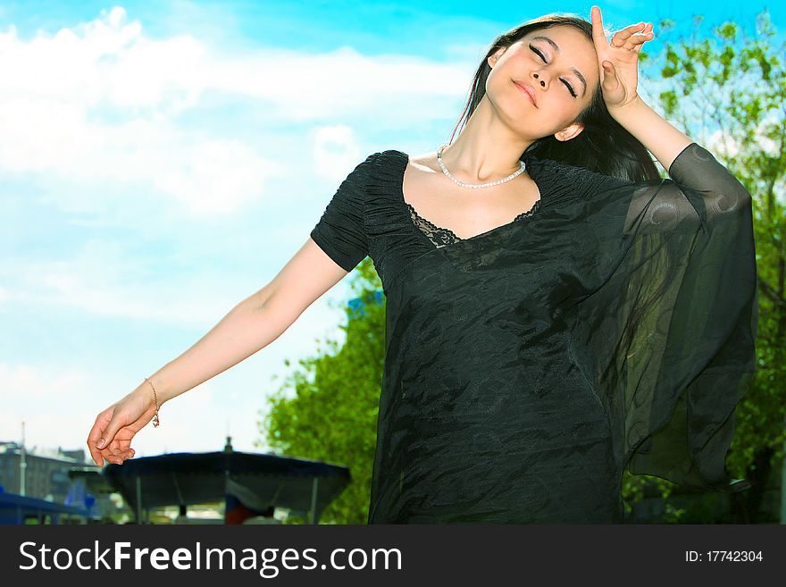 Beautiful Asian girl in a black dress and black shawl posing with eyes closed and your face to the wind