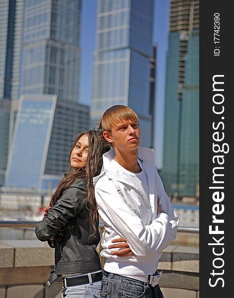Two fashionable and trendy teenagers against the blue sky and skyscrapers (modern buildings)