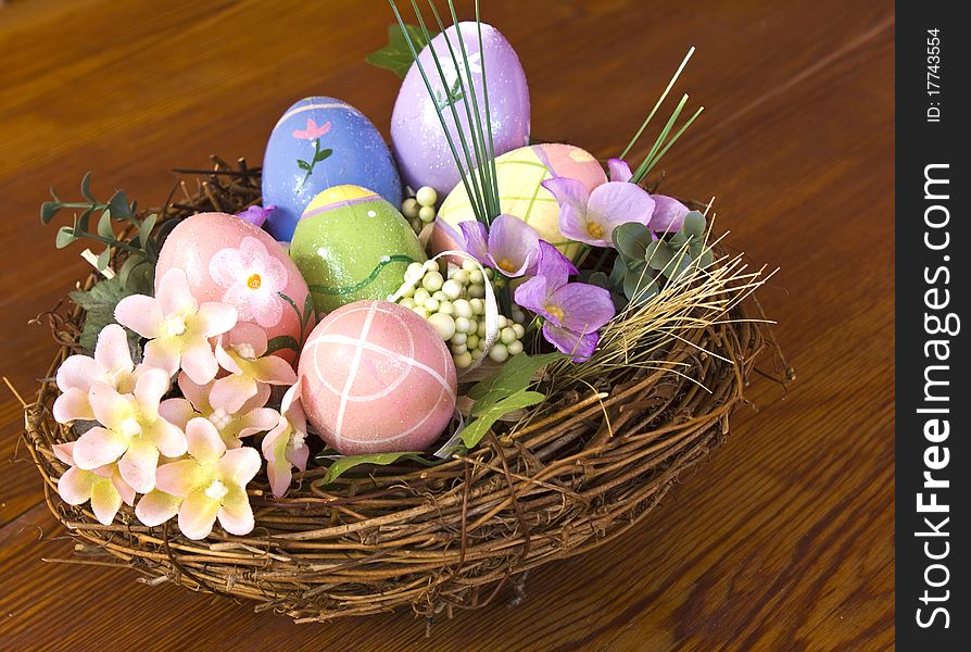 Painted Easter eggs in nest with flowers and side view on a wooden table