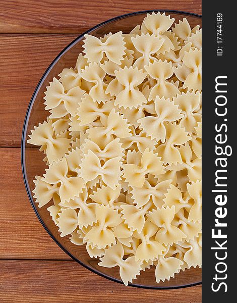 Raw farfalle in glass plate on wooden board. Raw farfalle in glass plate on wooden board